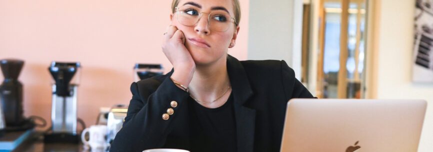 Junge Frau sitzt vor dem Computer und denkt nach, über grobe Fahrlässigkeit bei Versicherungen?